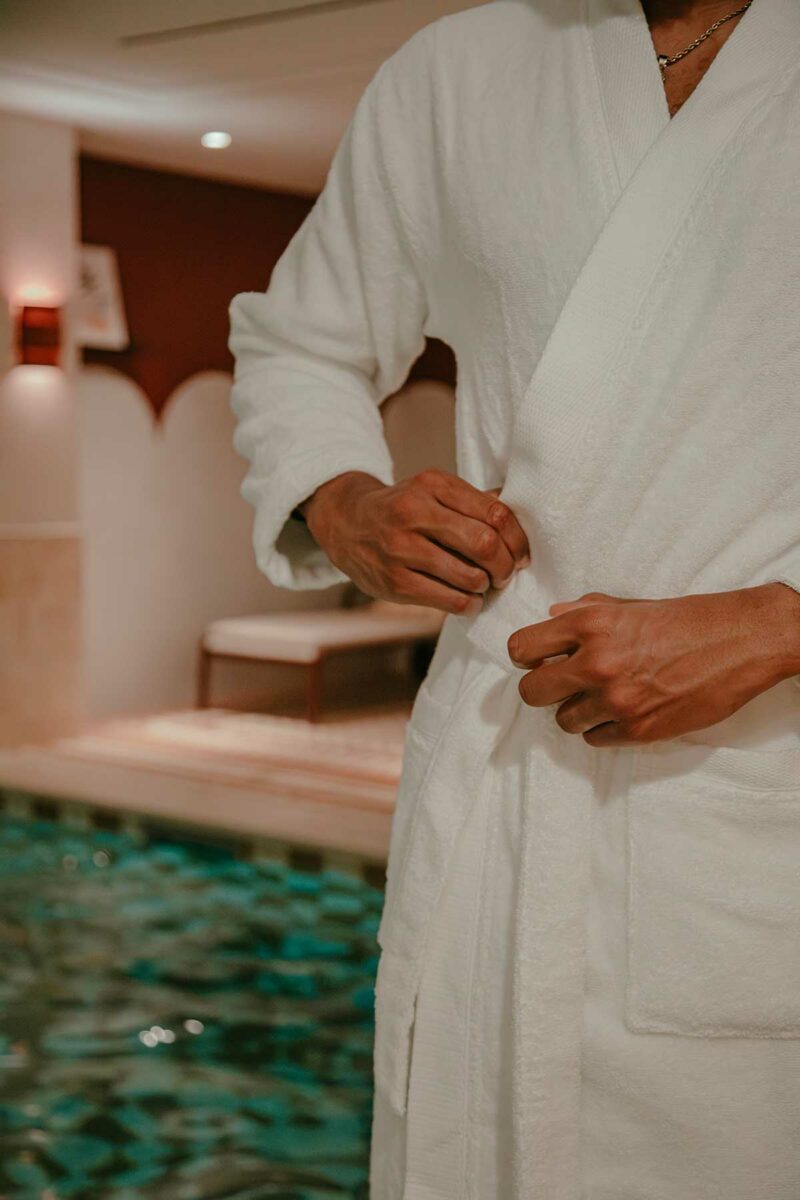 Homme nouant la ceinture du peignoir kimono Narumi Madura blanc dans un espace spa