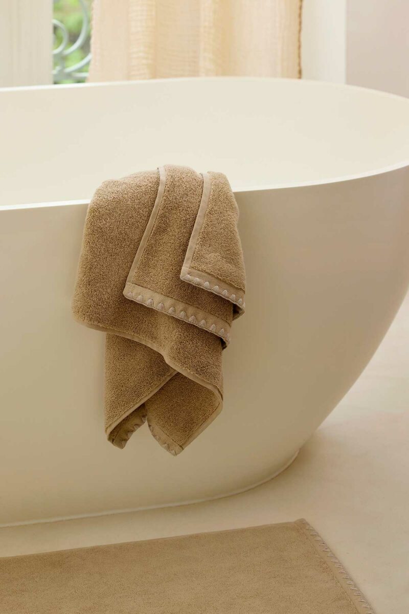 Serviette de bain Neryda Madura en beige lin drapée sur le bord d'une baignoire îlot