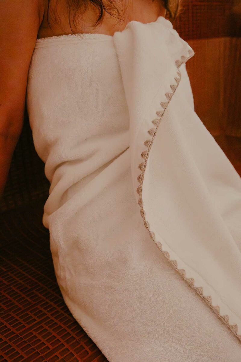 Femme enveloppée dans une serviette de bain Neryda Madura blanche avec point de feston, dans un sauna