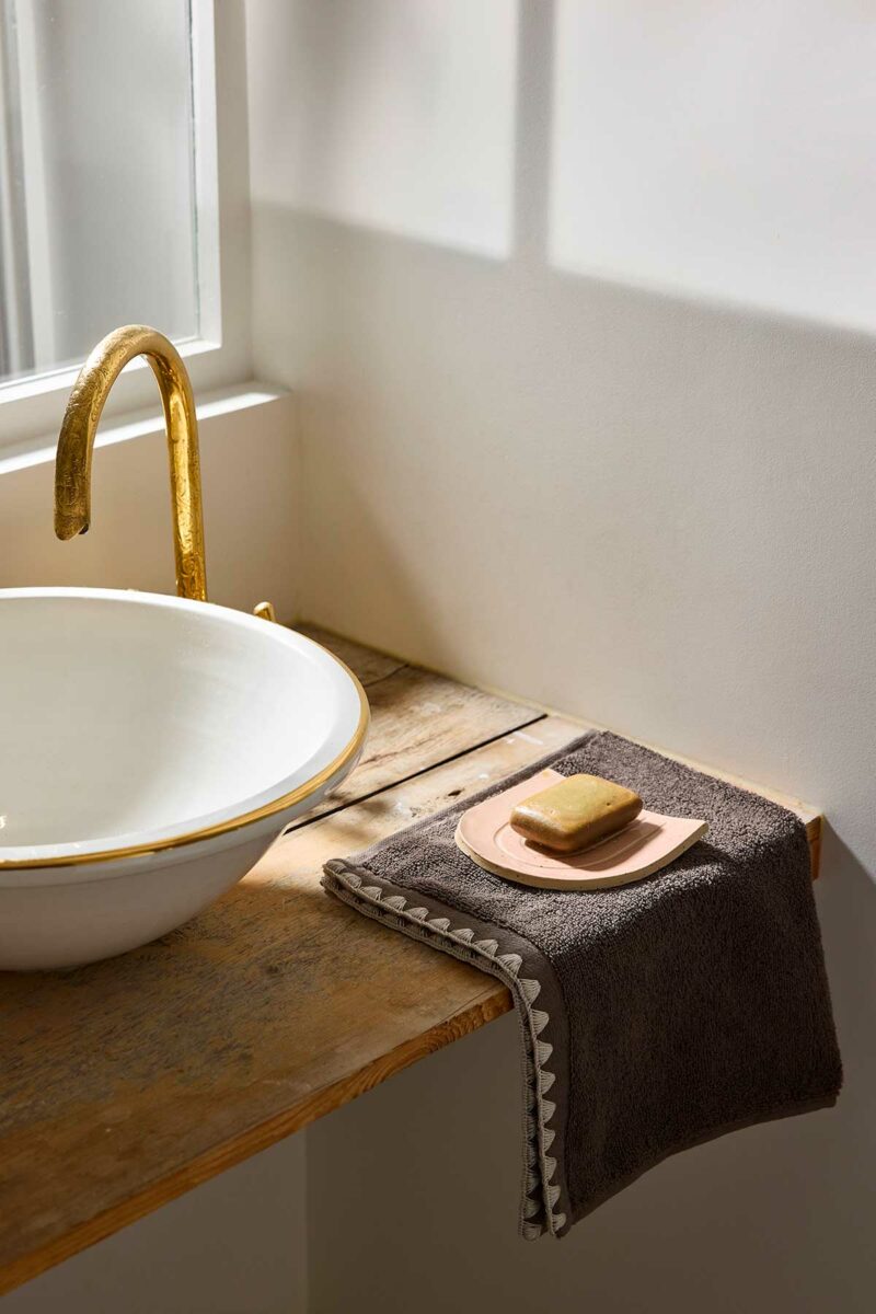 Serviette de bain Neryda Madura en brun cendré posée sur une console en bois avec un savon, à côté d'une vasque
