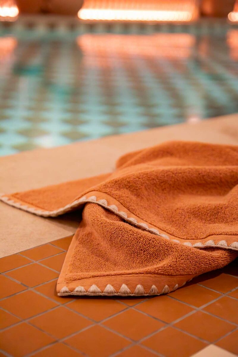 Serviette de bain Neryda Madura en terre d'argile posée au bord d'une piscine, détail du point de feston