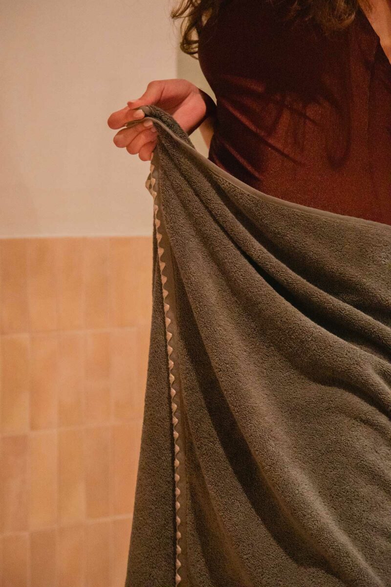 Femme tenant une serviette de bain Neryda Madura en vert séquoia, détail du point de feston triangulaire