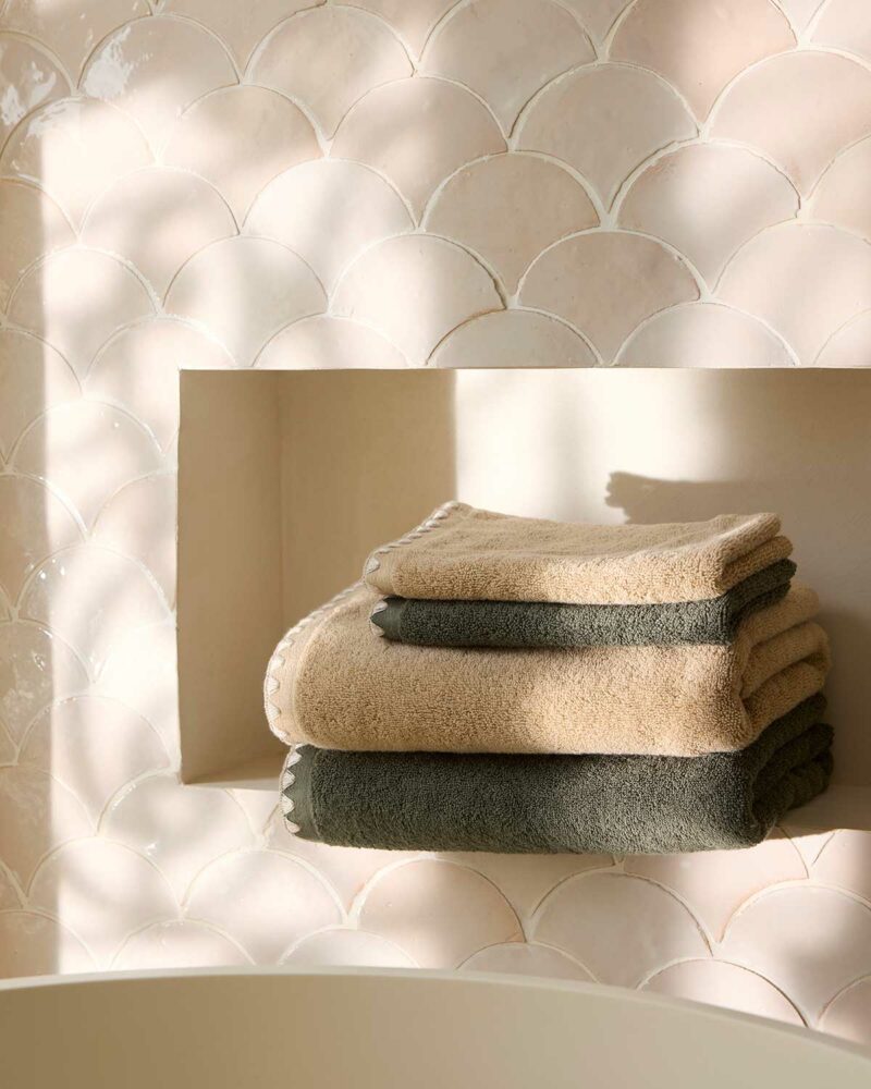 Serviettes de bain Neryda Madura en beige et vert séquoia disposées dans une niche en carrelage écaille