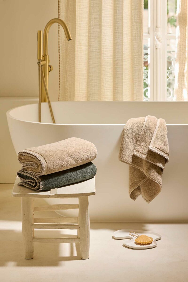 Serviettes de bain Neryda Madura empilées sur un tabouret dans une salle de bains lumineuse